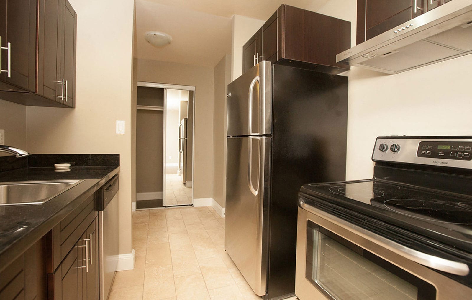 Galley kitchen with dark cabinetry, black counter and stainless steel refrigerator, range and dishwasher